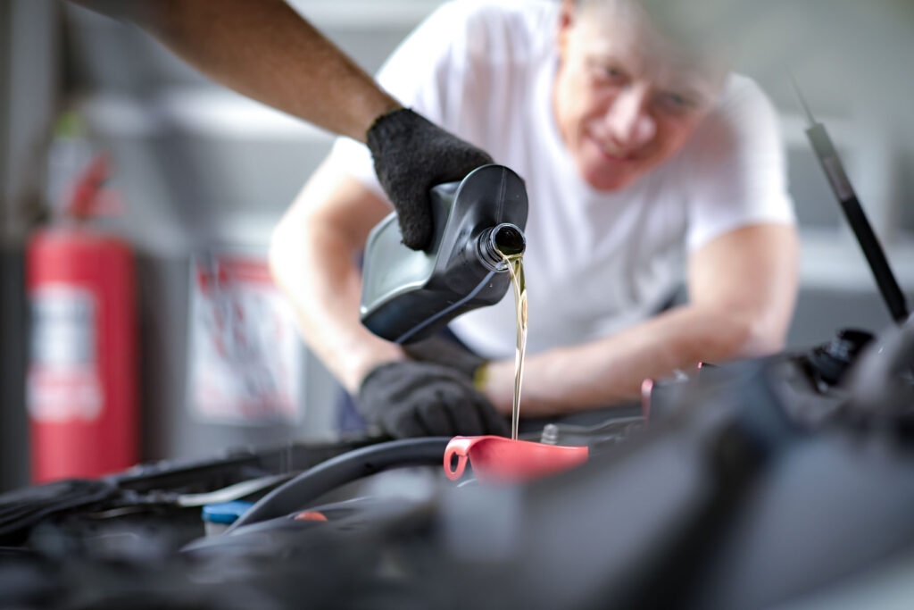 Der Mechaniker wechselt das Öl während er über die Motorhaube gebeugt ist.